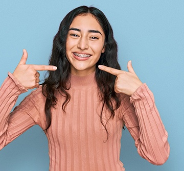 Teen girl smiling while pointing to her braces