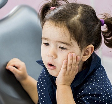 Little girl in dental chair holding cheek