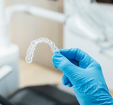 Dentist with blue glove holding clear aligner