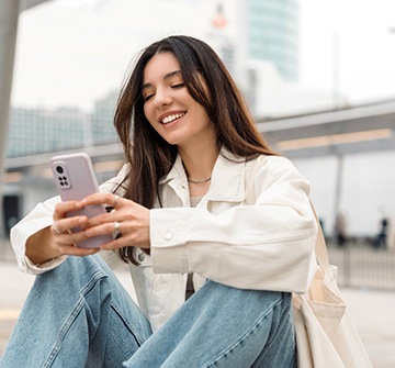 Teen girl smiling while looking at phone outside