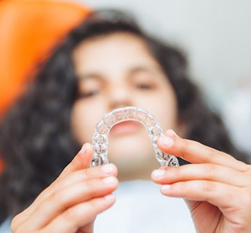 Teenage girl smiling while holding aligner in treatment chair