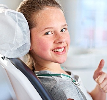 Young girl in dental chair giving thumbs up