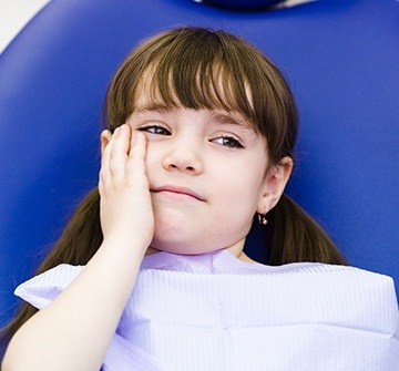 Girl in dental chair holding cheek