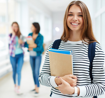 Smiling teen girl holding books in hallway