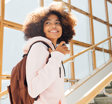 Teen girl with backpack smiling while walking upstairs
