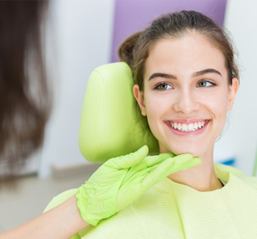 Orthodontist with green gloves looking at teen's smile