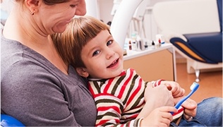 Mother holding child in lap in dental chair