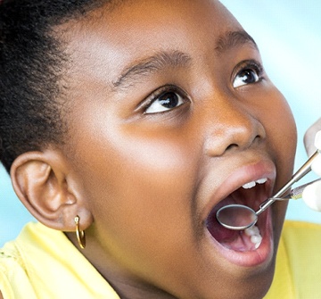 A little girl with gold earrings opening her mouth to show her dentist the problem area of her mouth