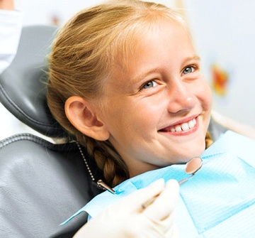 A smiling blonde-haired little girl having her teeth checked at the dentist’s office
