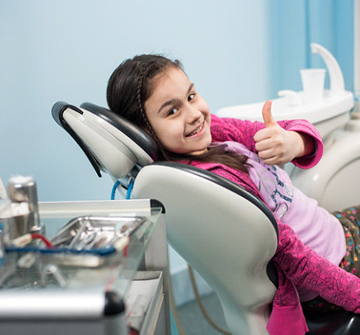 A young girl lying back in a dentist’s chair and giving a thumbs up after undergoing emergency dentistry