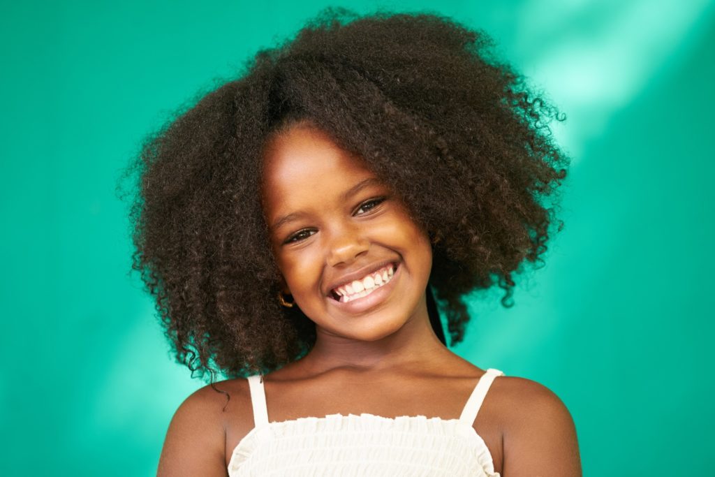 Young girl with curly hair and healthy teeth smiling