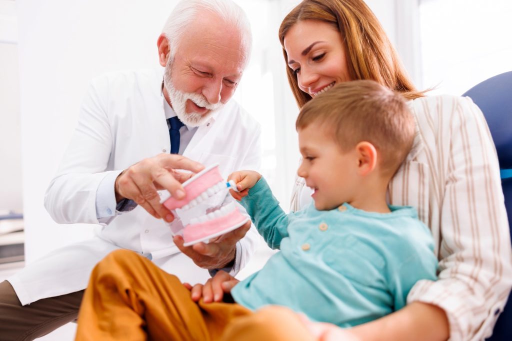 Dentist showing child how to brush on model of teeth